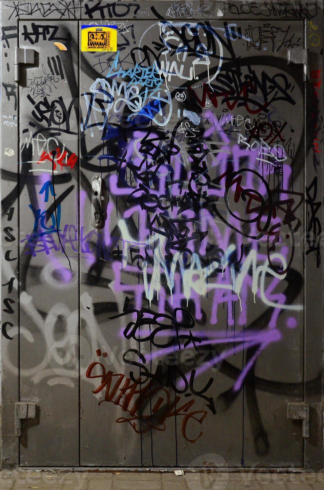 Fragment of graffiti tags. The old wall is spoiled with paint stains in the style of street art culture. Painted metal door photo