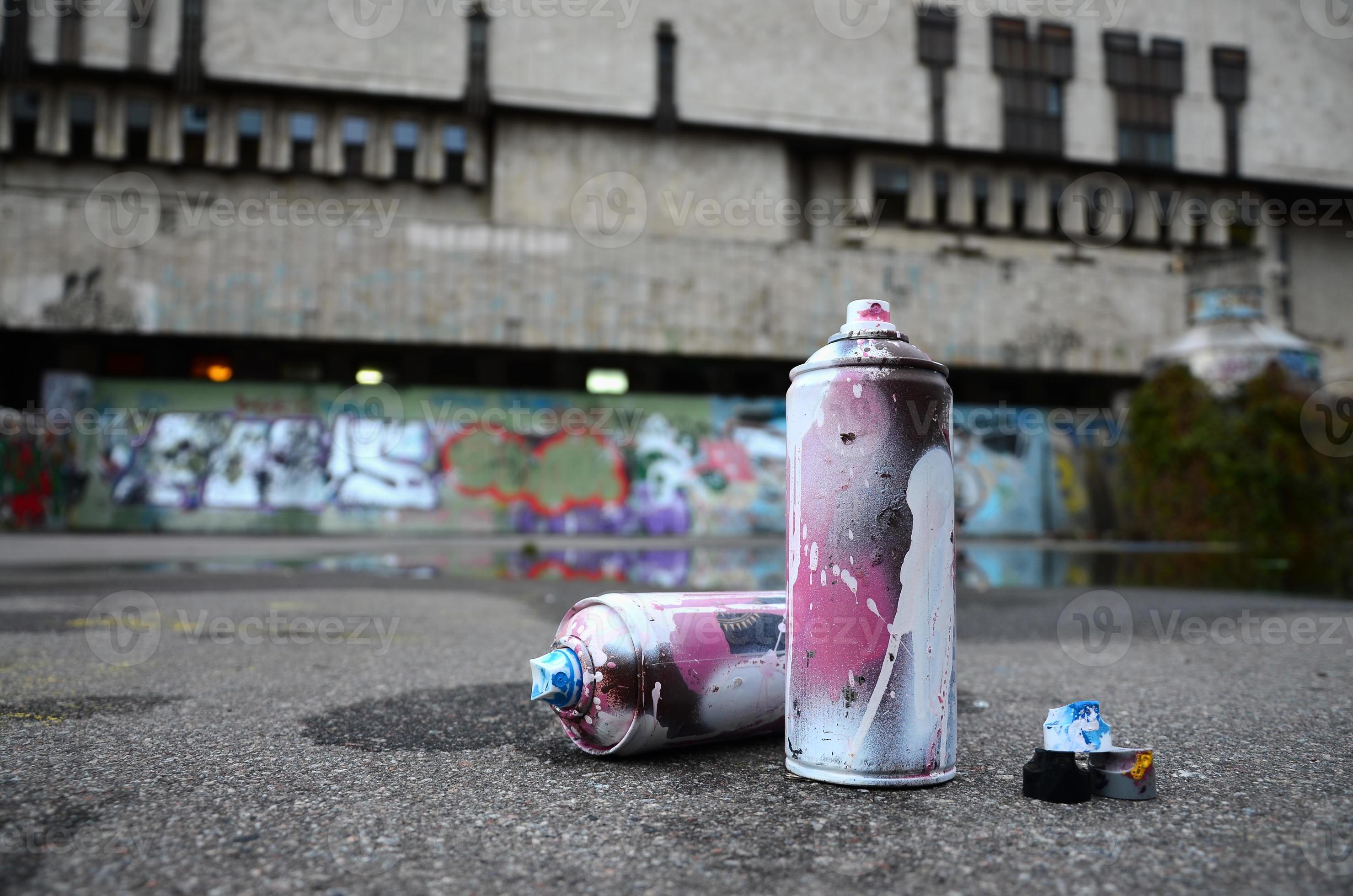 Several used spray cans with pink and white paint and caps for spraying