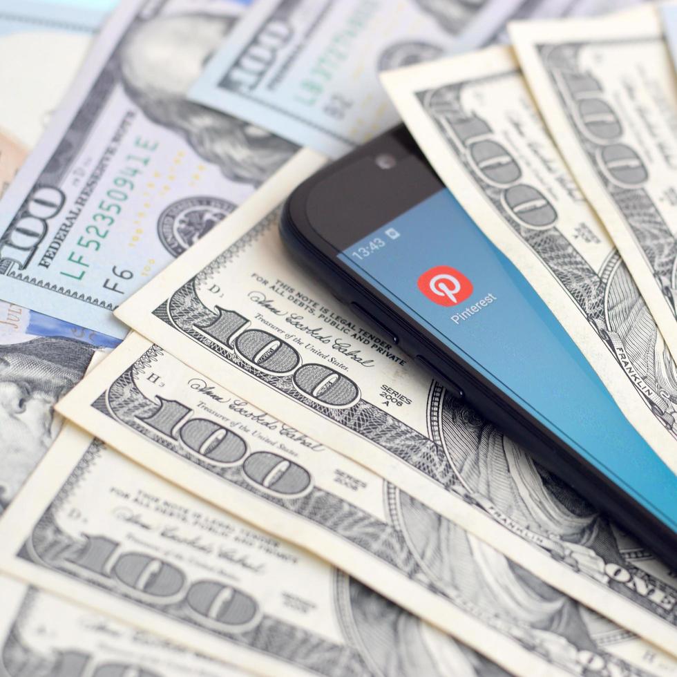 Smartphone screen with Pinterest app and lot of hundred dollar bills. Business and social networking concept photo