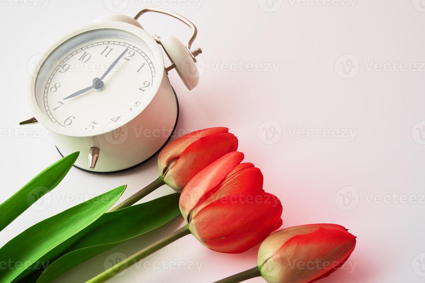Alarm clock and flowers in vase on white background photo