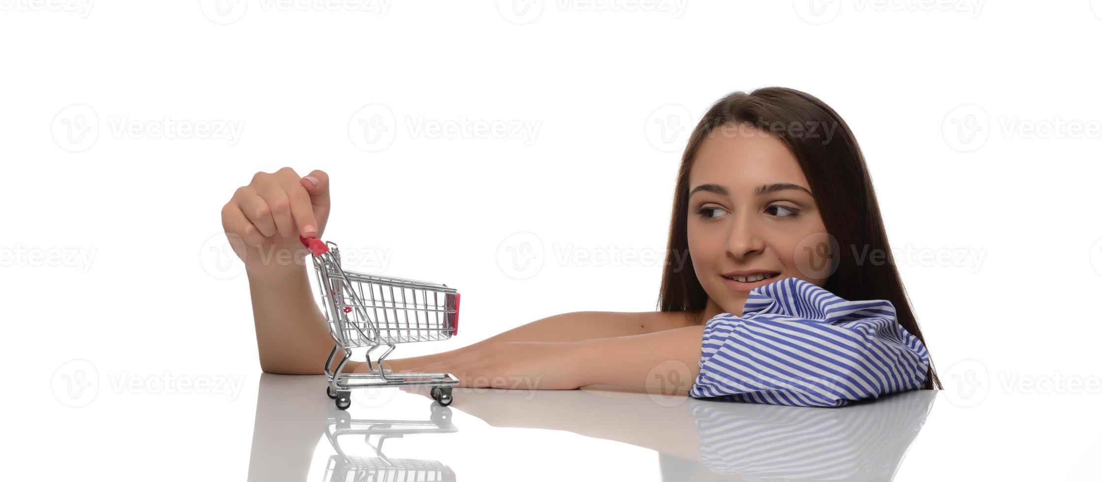 Woman thought about shopping. Girl is thinking about shopping. Woman chooses where to make purchase. Woman shopper with mini trolley from supermarket. photo