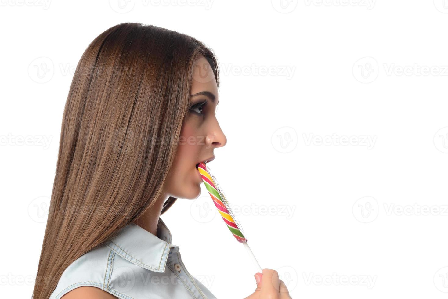 mujer lamiendo caramelos. modelo femenino comiendo deliciosa paleta de confitería con expresión sorprendida. tiro del estudio aislado fondo blanco foto