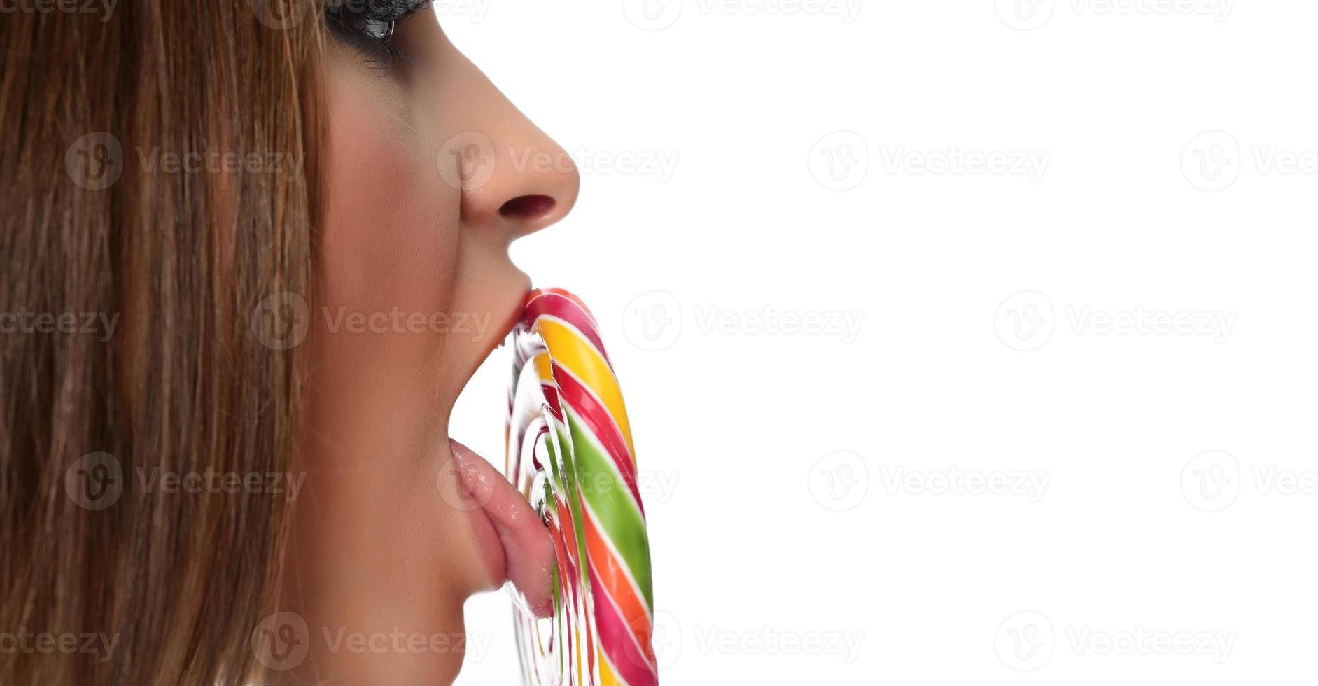 woman licking sweet candy. Female model eating delicious confectionery lollipop with surprised expression. studio shot isolated white background photo