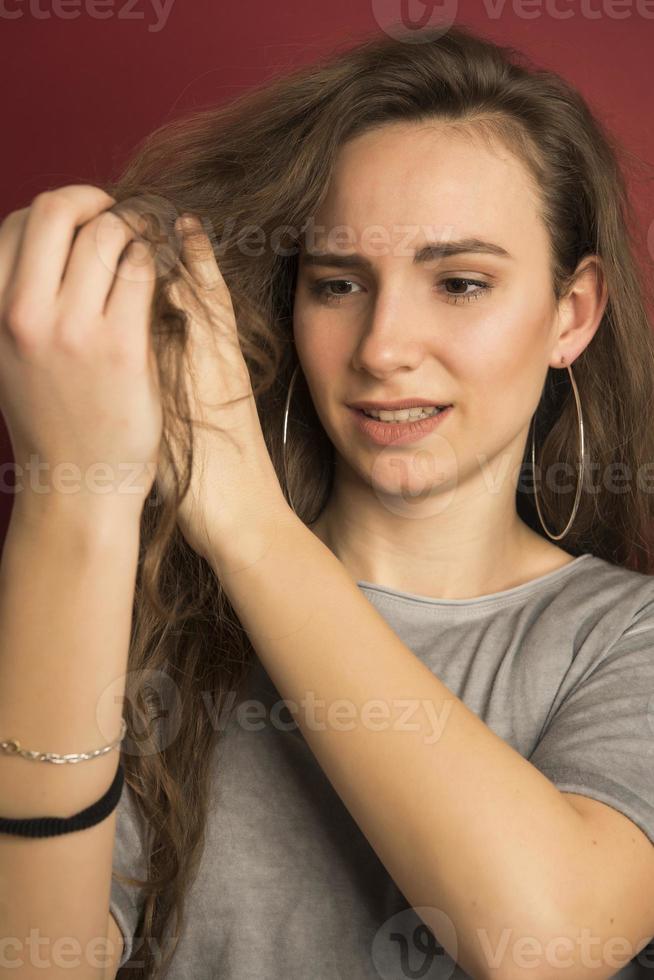 cabello dañado. hermosa joven triste con el pelo largo y desaliñado. retrato de primer plano de una modelo femenina sosteniendo el cabello seco sin cepillar en las manos. concepto de daños al cabello, salud y belleza. alta resolución foto