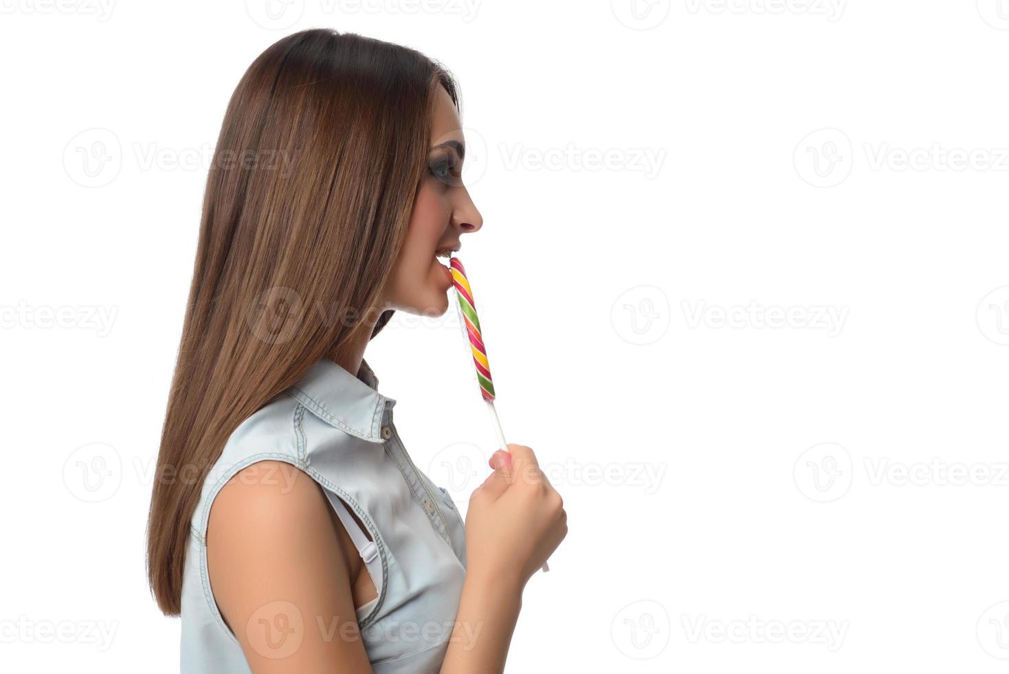 mujer lamiendo caramelos. modelo femenino comiendo deliciosa paleta de confitería con expresión sorprendida. tiro del estudio aislado fondo blanco foto