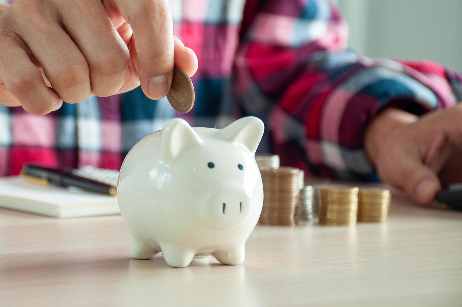 Close-up of a man's hand putting money into a piggy bank to save After calculating the costs. Concepts of saving money, financial, accounting photo