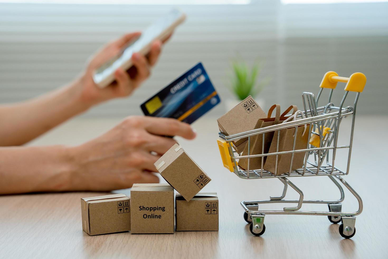 Online shopping-boxes or parcels are placed on the table and shopping carts. Blurred background, woman use credit card to make online purchases on laptop. Online service. New normal shopping delivery. photo