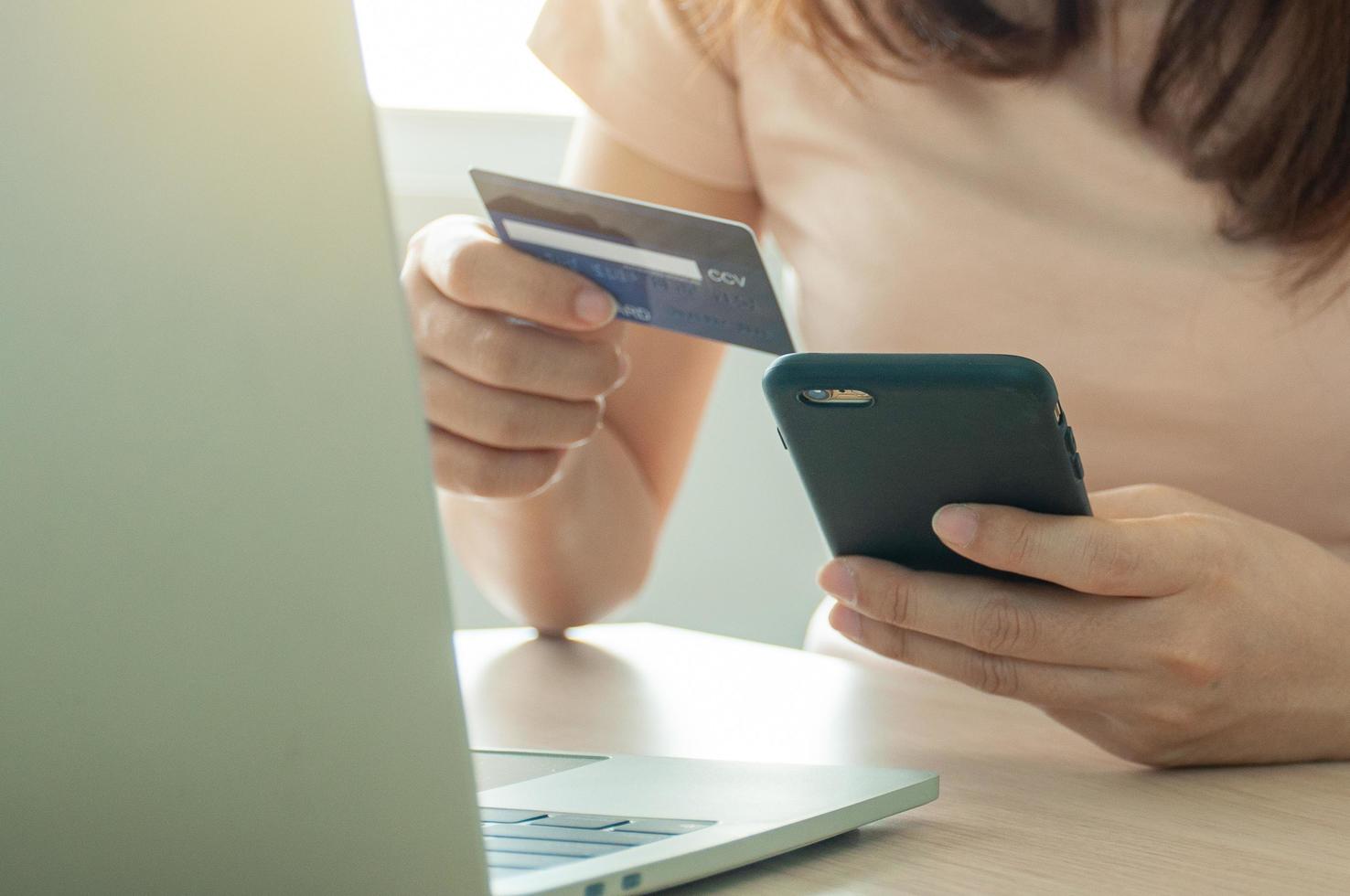 Female hands using smartphone and laptop computer for online shopping at home. Hand holding mobile phone with payment detail page display and credit card, Online shopping and stay home concepts. photo