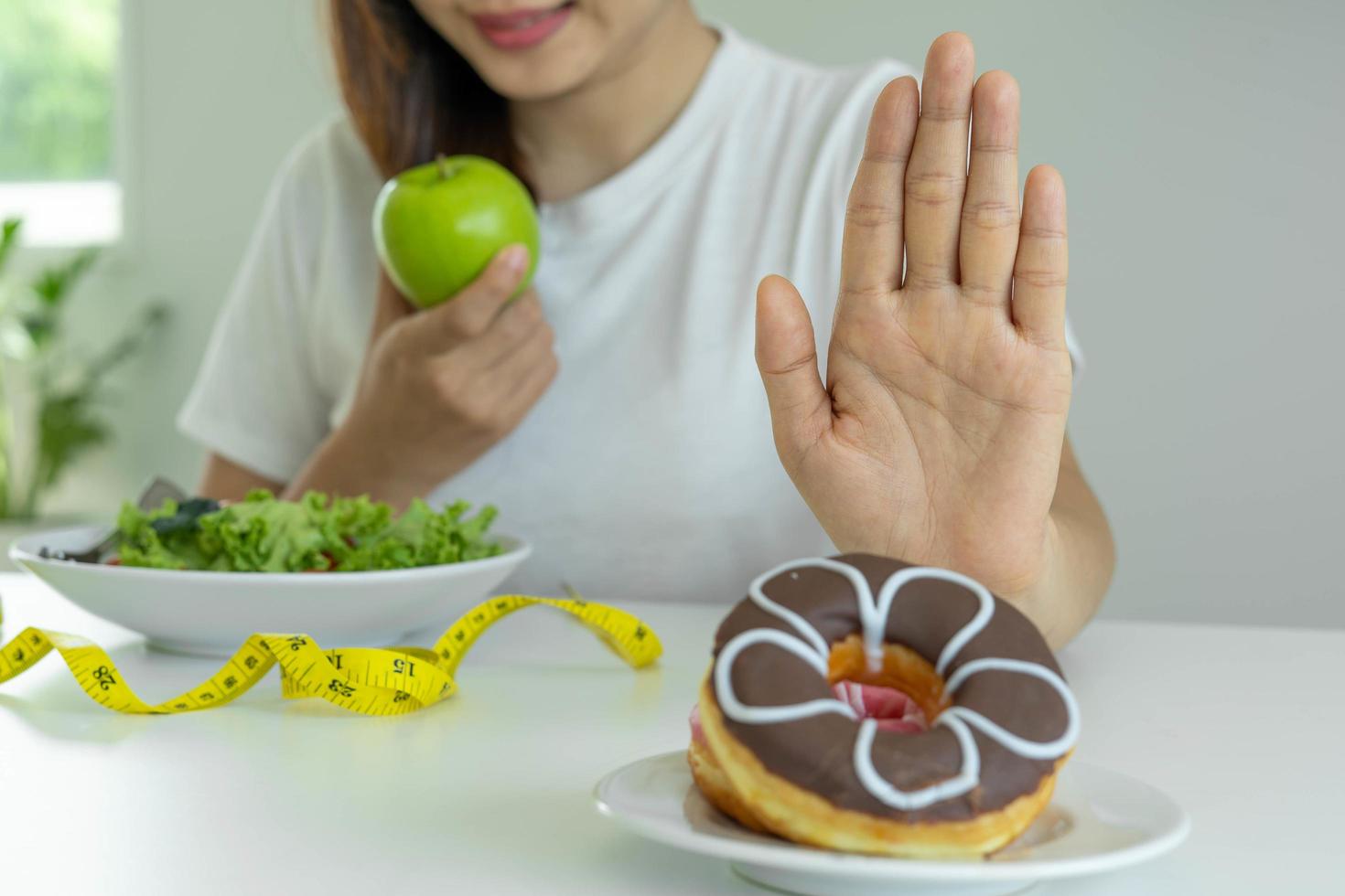 Women reject junk food or unhealthy foods such as doughnuts and choose healthy foods such as green apples and salads. Concept of fasting and good health. photo