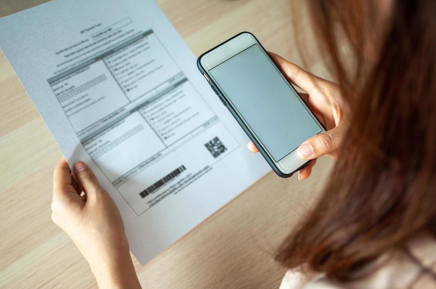 A woman uses a smartphone to scan the barcode to pay monthly phone bills after receiving an invoice sent to home. Online bill payment concept photo