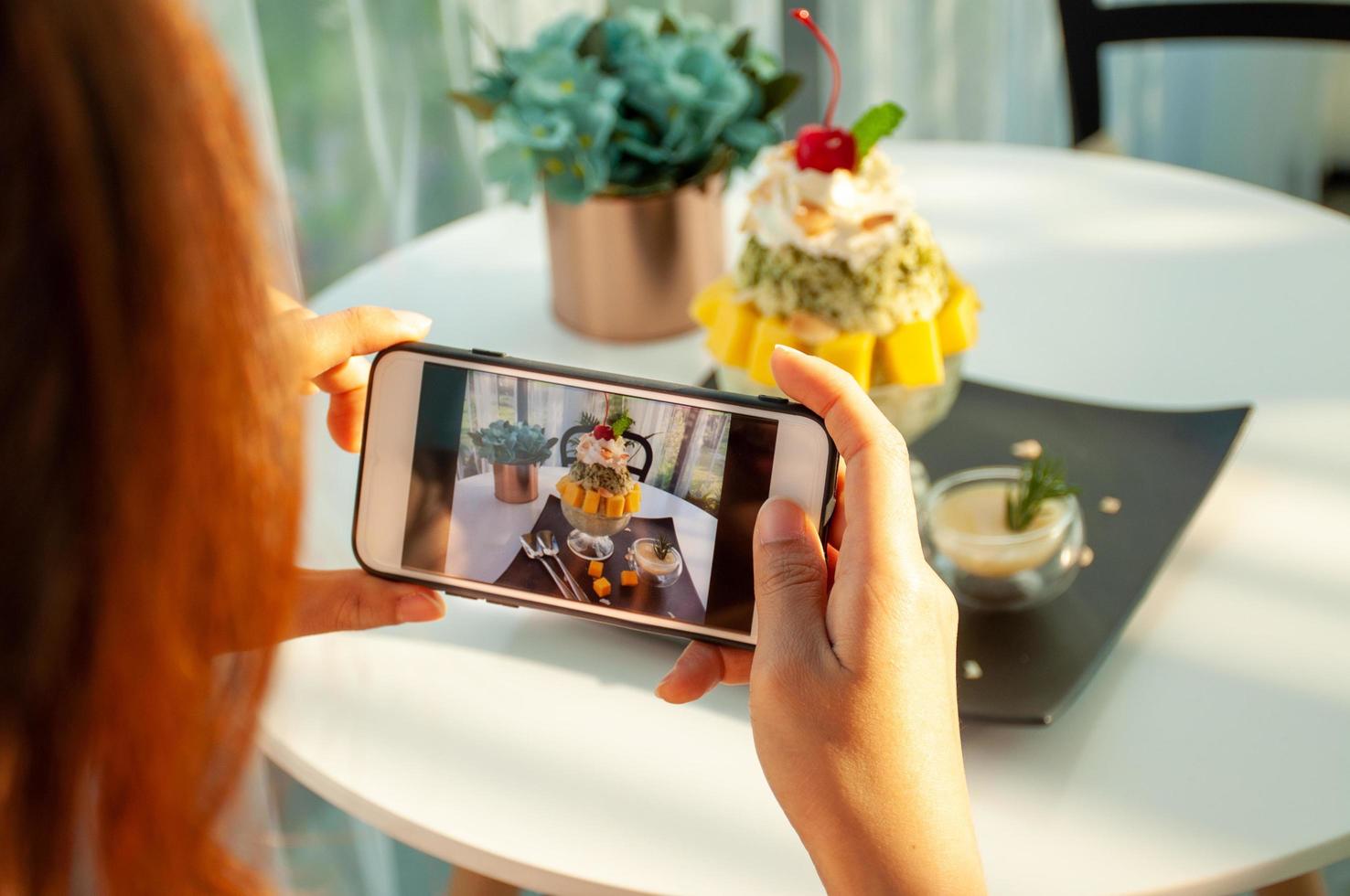 An Asian woman takes a picture of an ice-mango in a cafe and prepares to upload it to a social app. photo