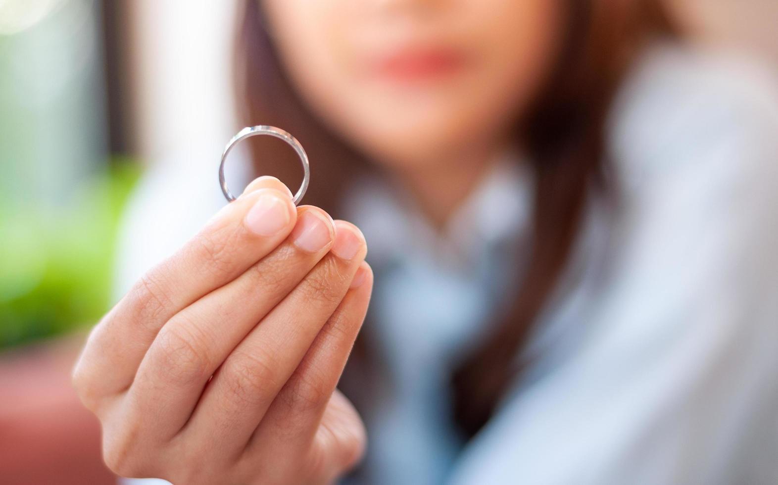 Close up of a single sad wife after divorce lamenting holding the wedding ring in a house interior. photo