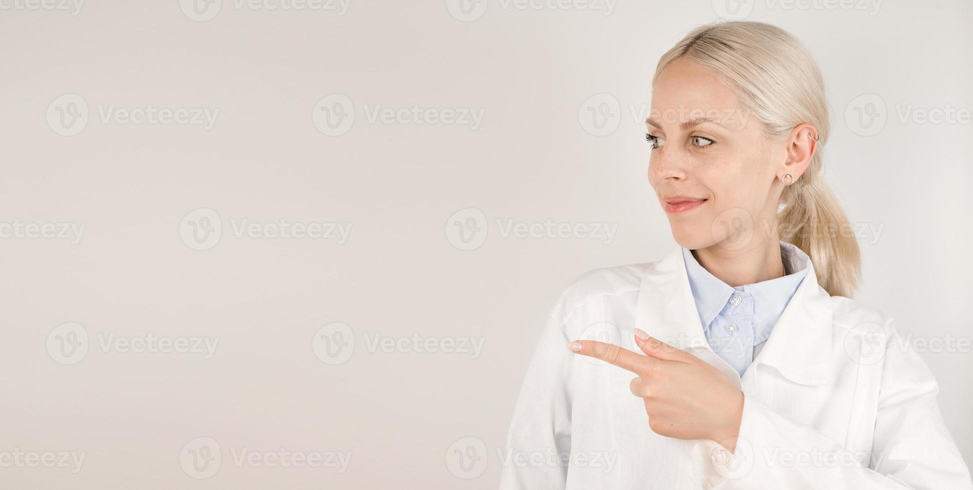 Professional smiling, attractive female doctor in medical coat painting at empty space. Copy space banner. Place for text photo