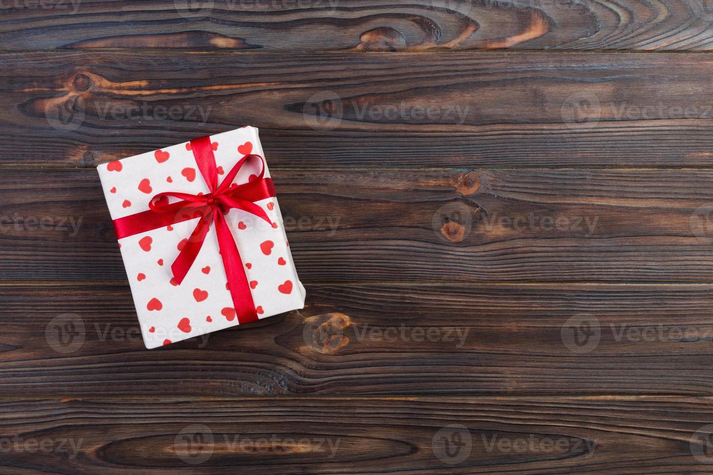 Valentine or other holiday handmade present in paper with red hearts and gifts box in holiday wrapper. Present box of gift on Dark wooden table top view with copy space, empty space for design photo