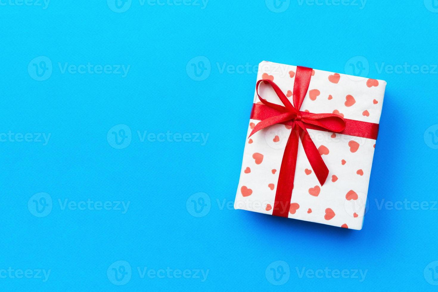 Gift box with red ribbon and heart on blue background, top view with copy space for text photo