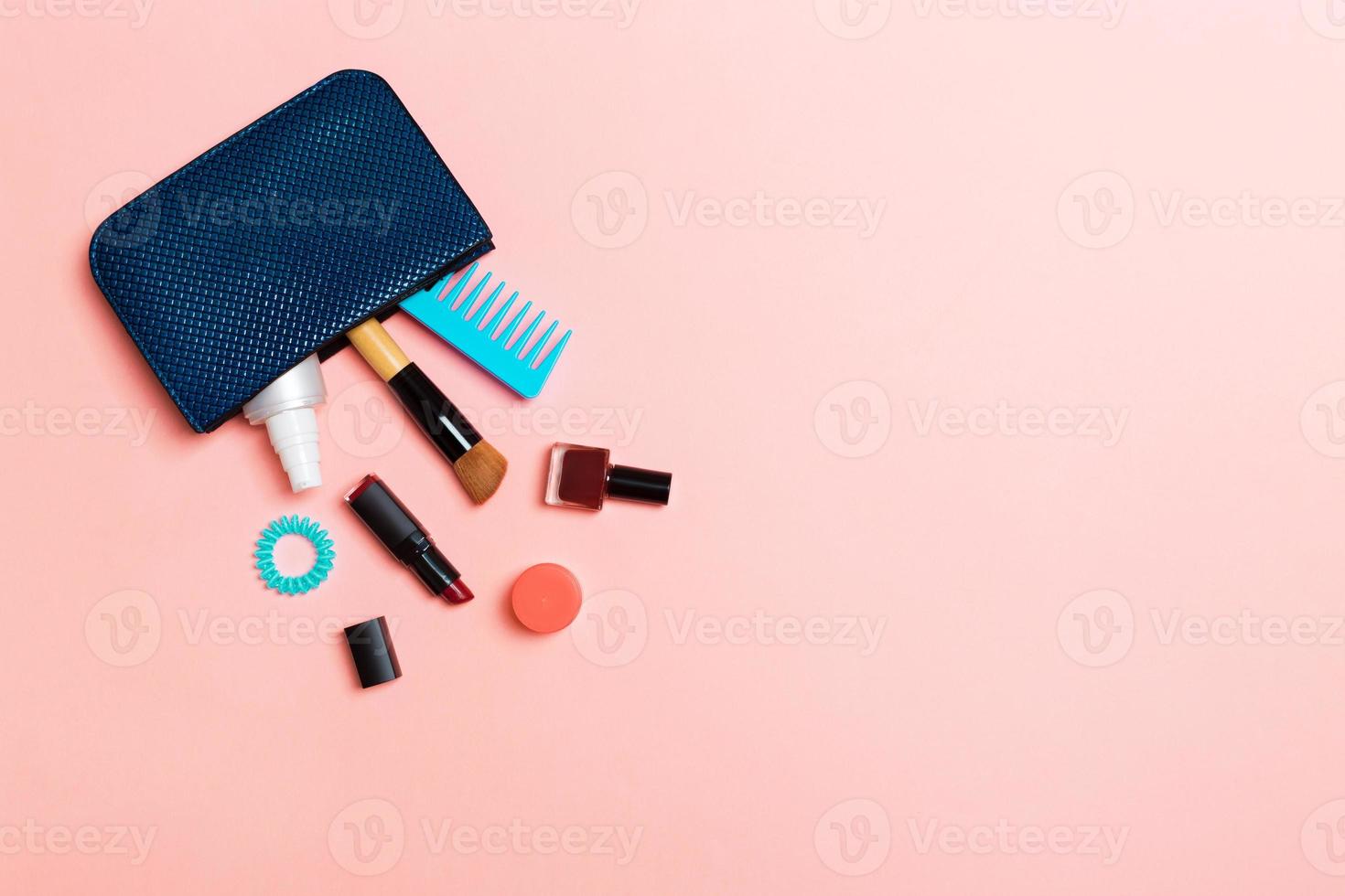 Make up products spilling out of cosmetics bag, on pink pastel background with empty space for your design photo