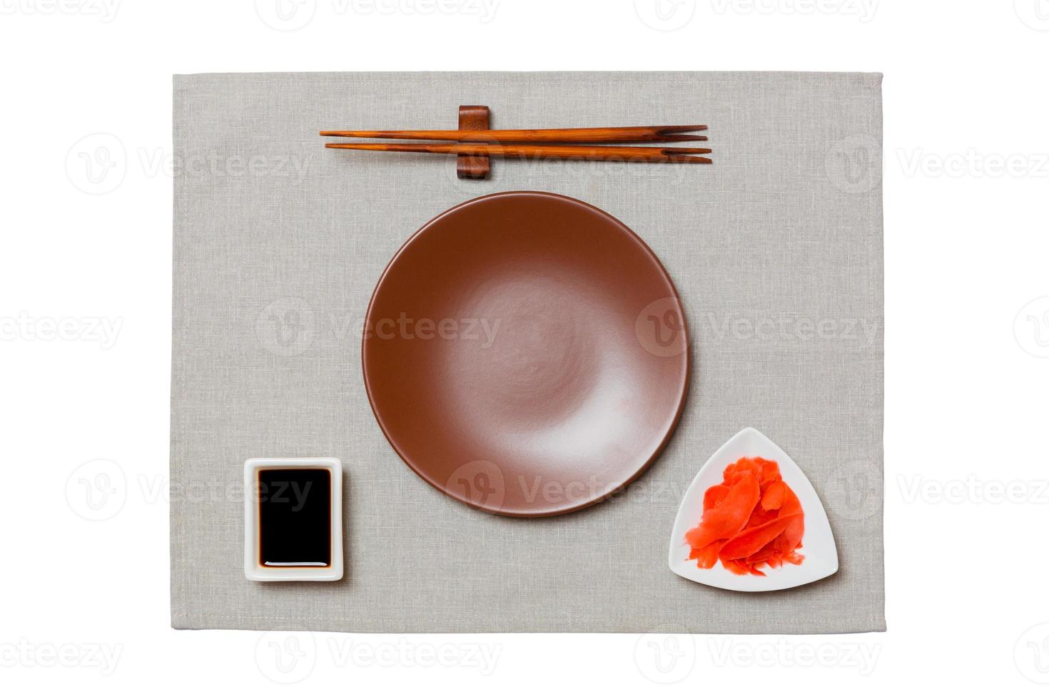 Empty round brown plate with chopsticks for sushi, ginger and soy sauce on grey napkin background. Top view with copy space for you design photo
