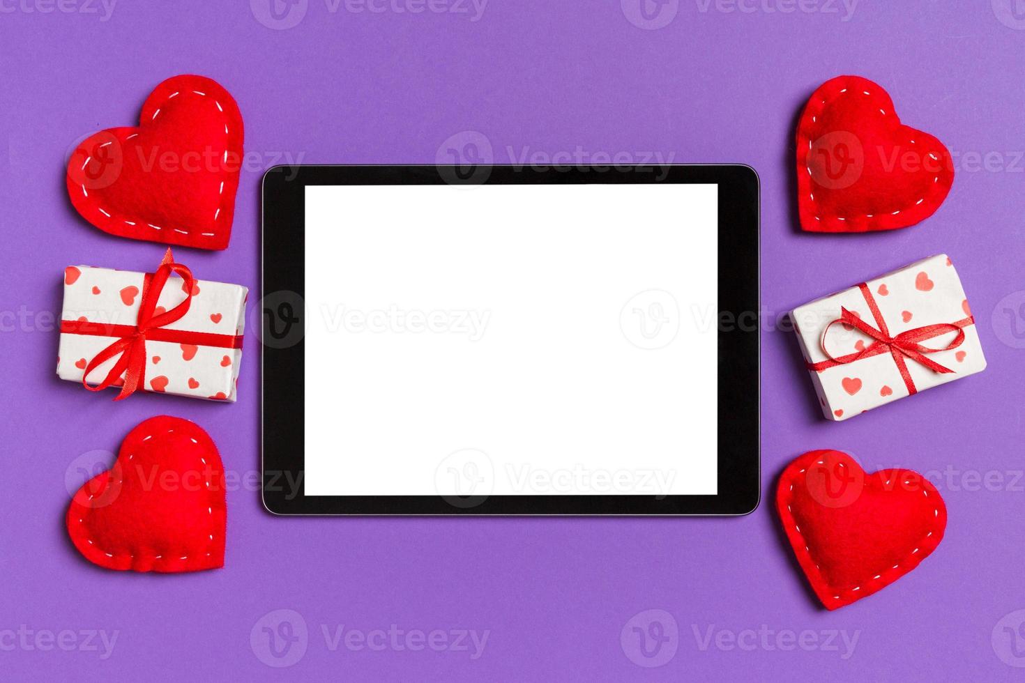 Top view of digital tablet surrounded with gift boxes and hearts on colorful background. Saint Valentine's day photo