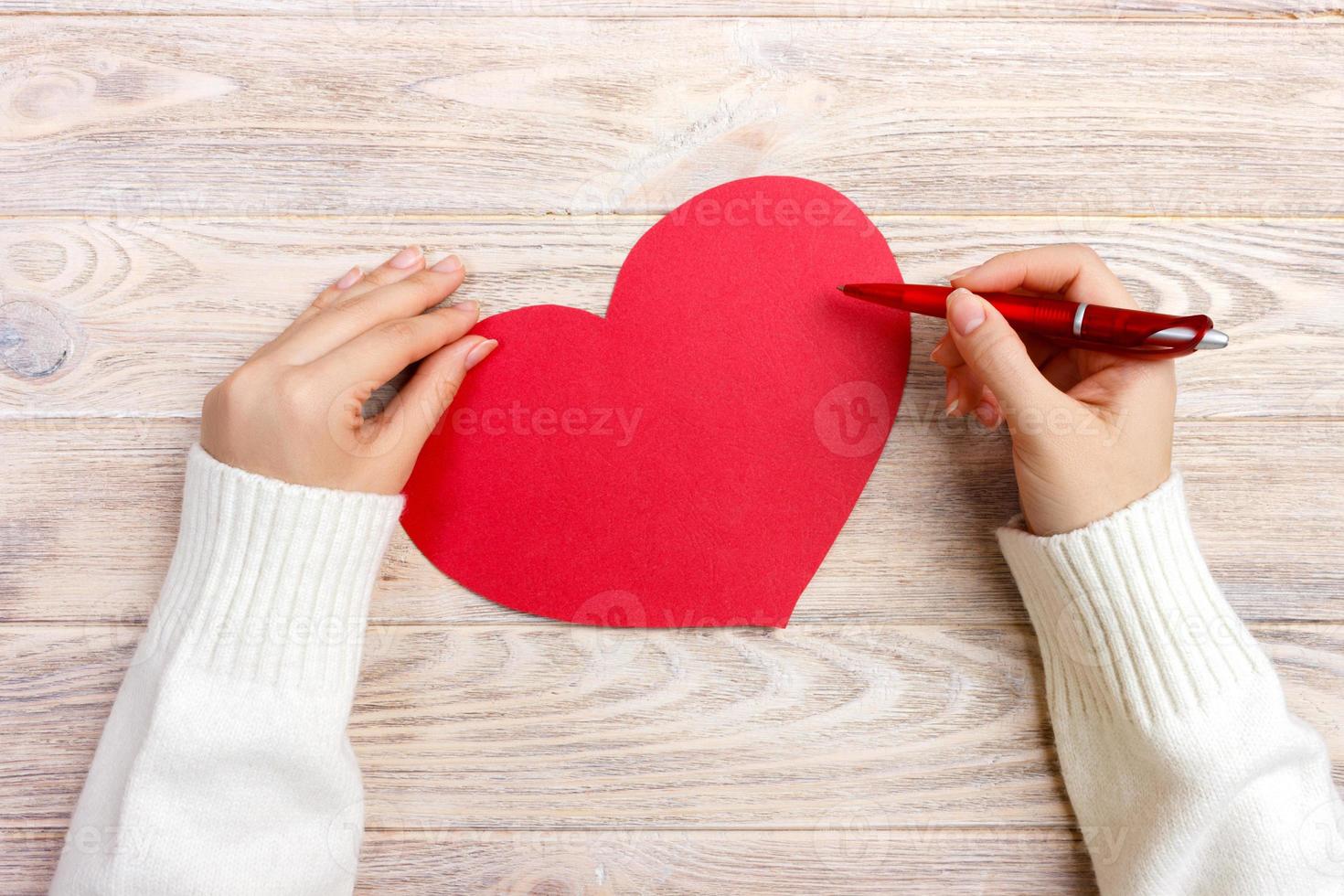 Hand of girl writing love letter on Valentine Day. Handmade red heart postcard. Woman write on postcard for 14 February holiday celebration. Flat lay. Top view photo