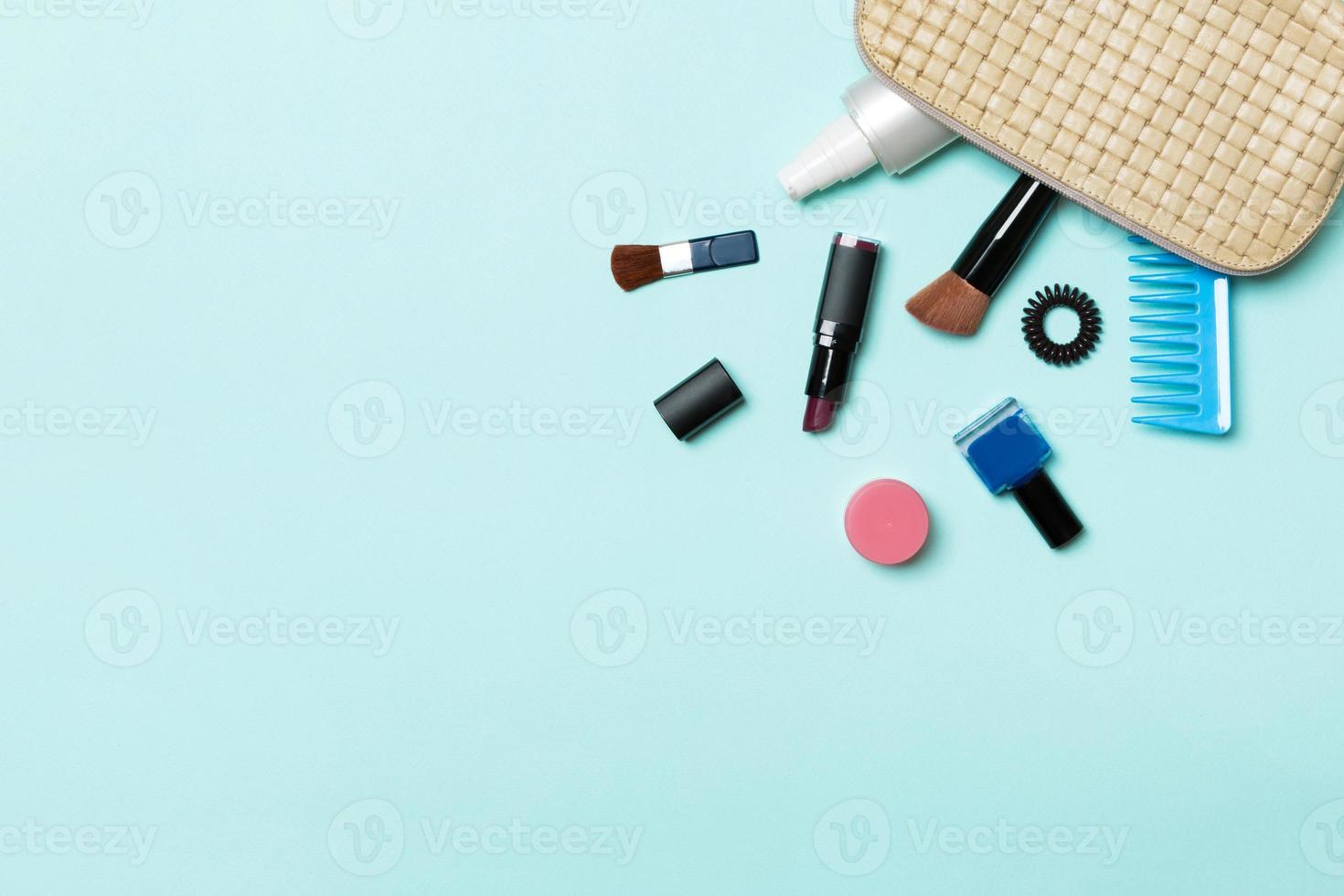 vista superior de los productos de maquillaje caídos de la bolsa de cosméticos sobre fondo azul. concepto cosmético con espacio para tu diseño foto