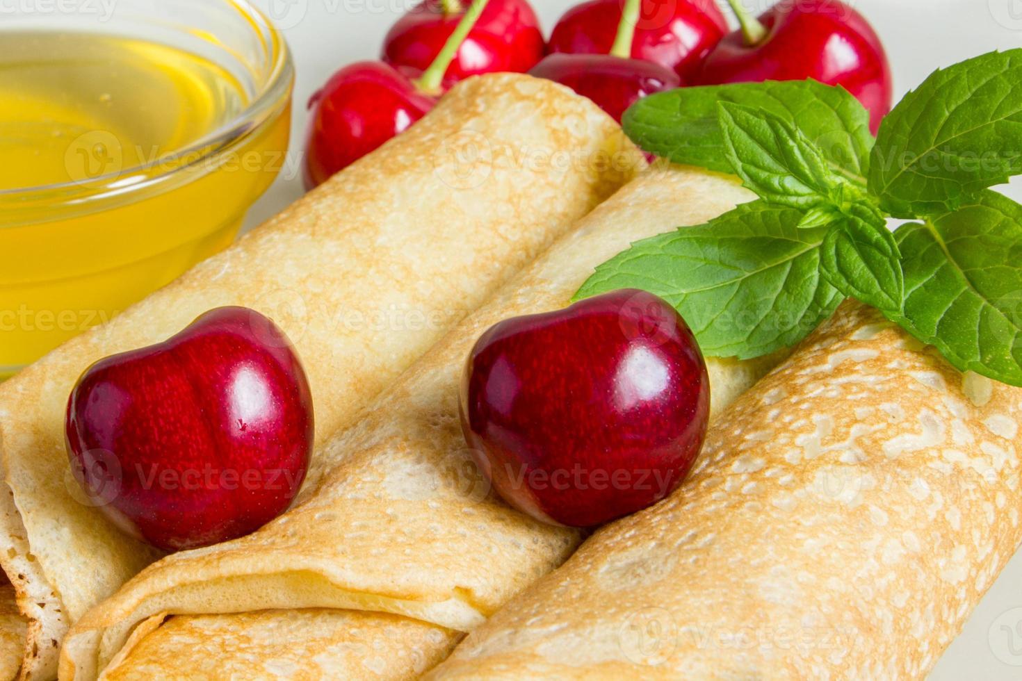 Homemade dessert. Fried pancakes with honey. Crepe with cherry on white plate background. photo