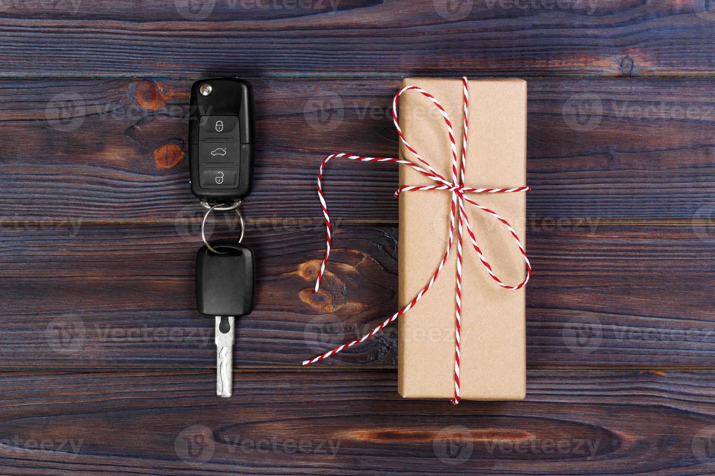 Car key near paper box with red ribbon bow on wooden table background. Christmas or Valentine's Day gift or present abstract concept photo
