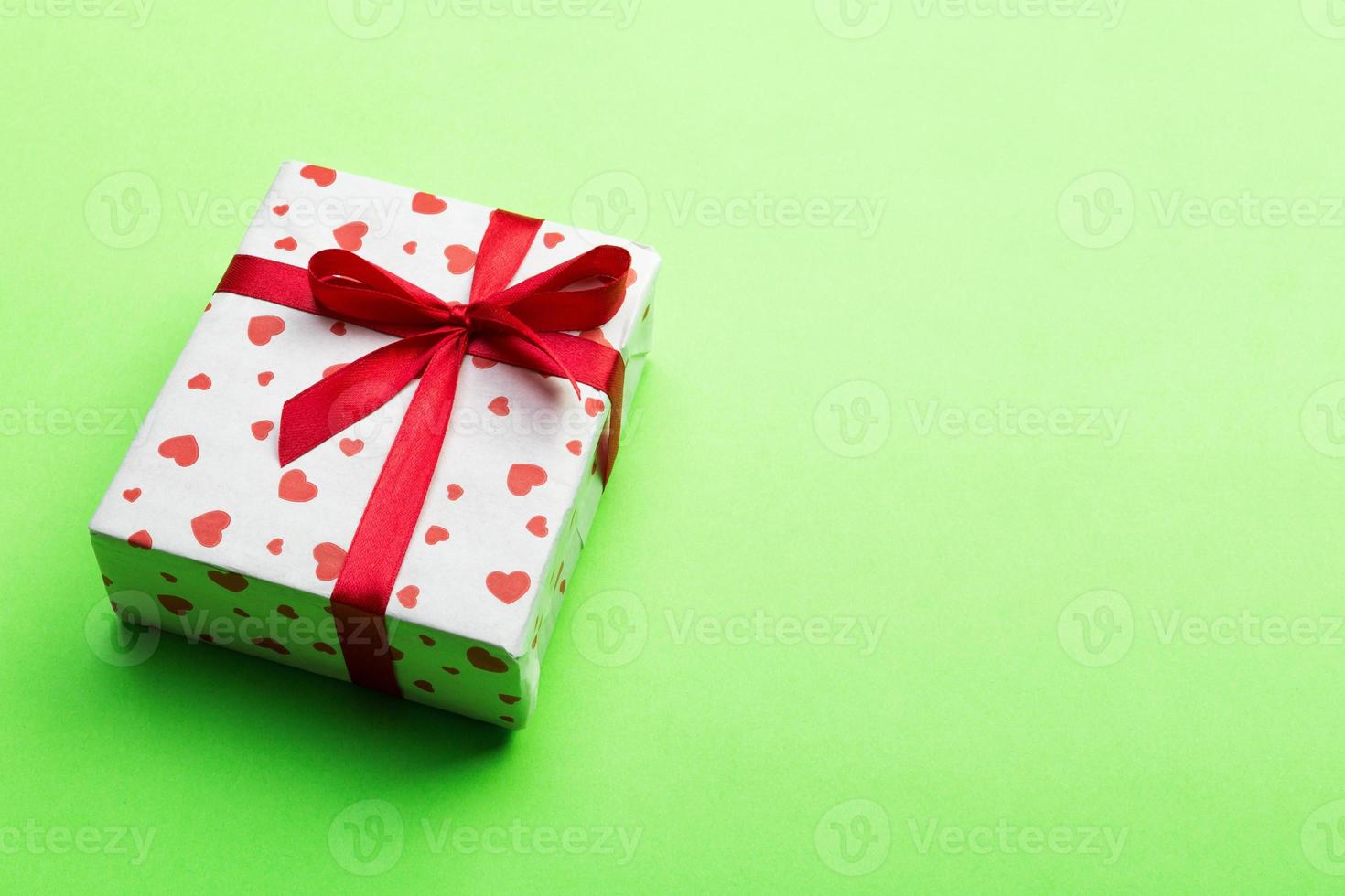 san valentín u otro regalo hecho a mano de vacaciones en papel con corazones rojos y caja de regalos en envoltorio de vacaciones. presente caja de regalo en la vista superior de la mesa de color verde con espacio de copia, espacio vacío para el diseño foto