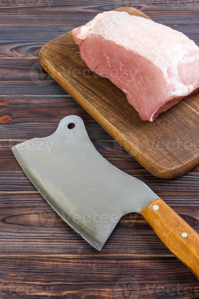 fresh large piece of pork on a wooden cutting board with kitchen ax. Top view on gray concrete background photo