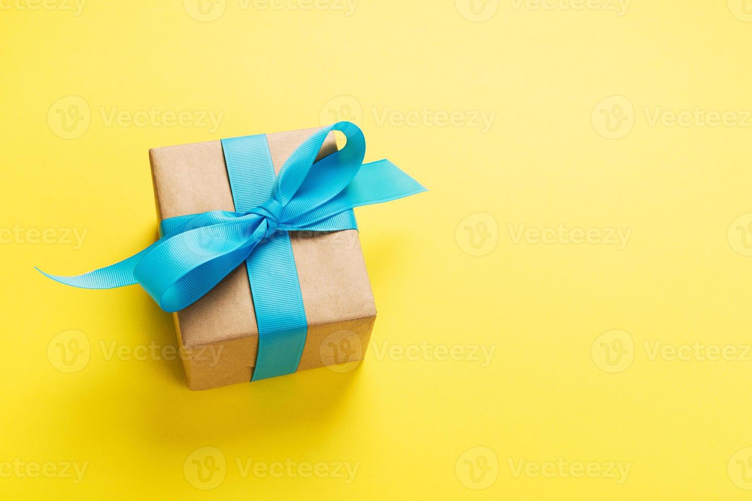 gift wrapped and decorated with blue bow on yellow background with copy space. Flat lay, top view photo