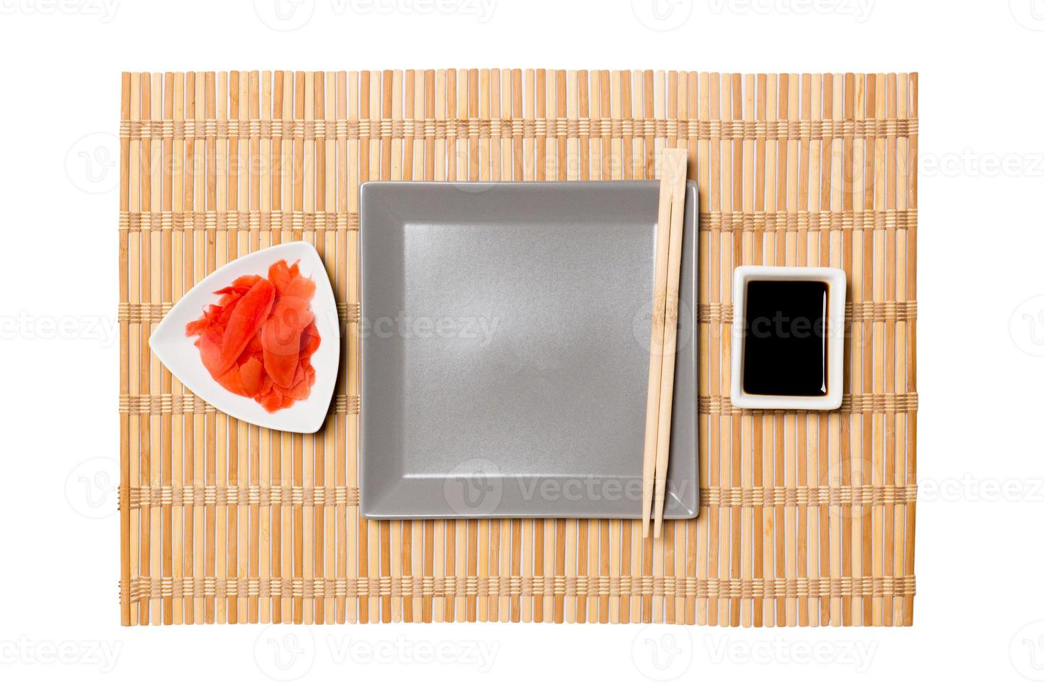 Empty gray square plate with chopsticks for sushi, ginger and soy sauce on yellow bamboo mat background. Top view with copy space for you design photo