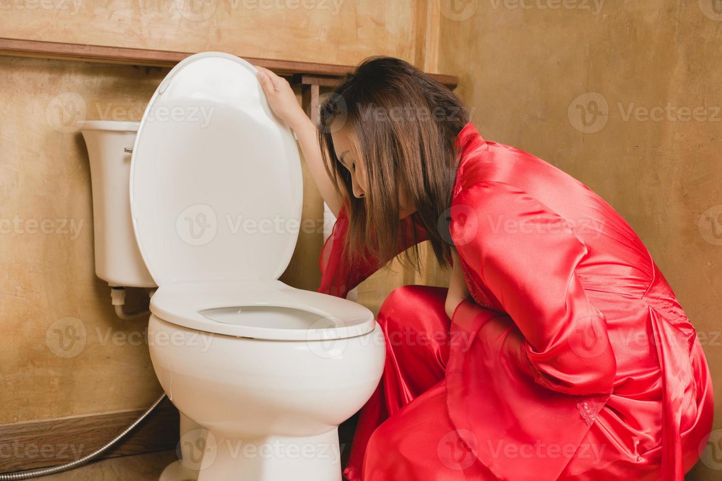 A woman in a red nightgown vomiting in the bathroom photo