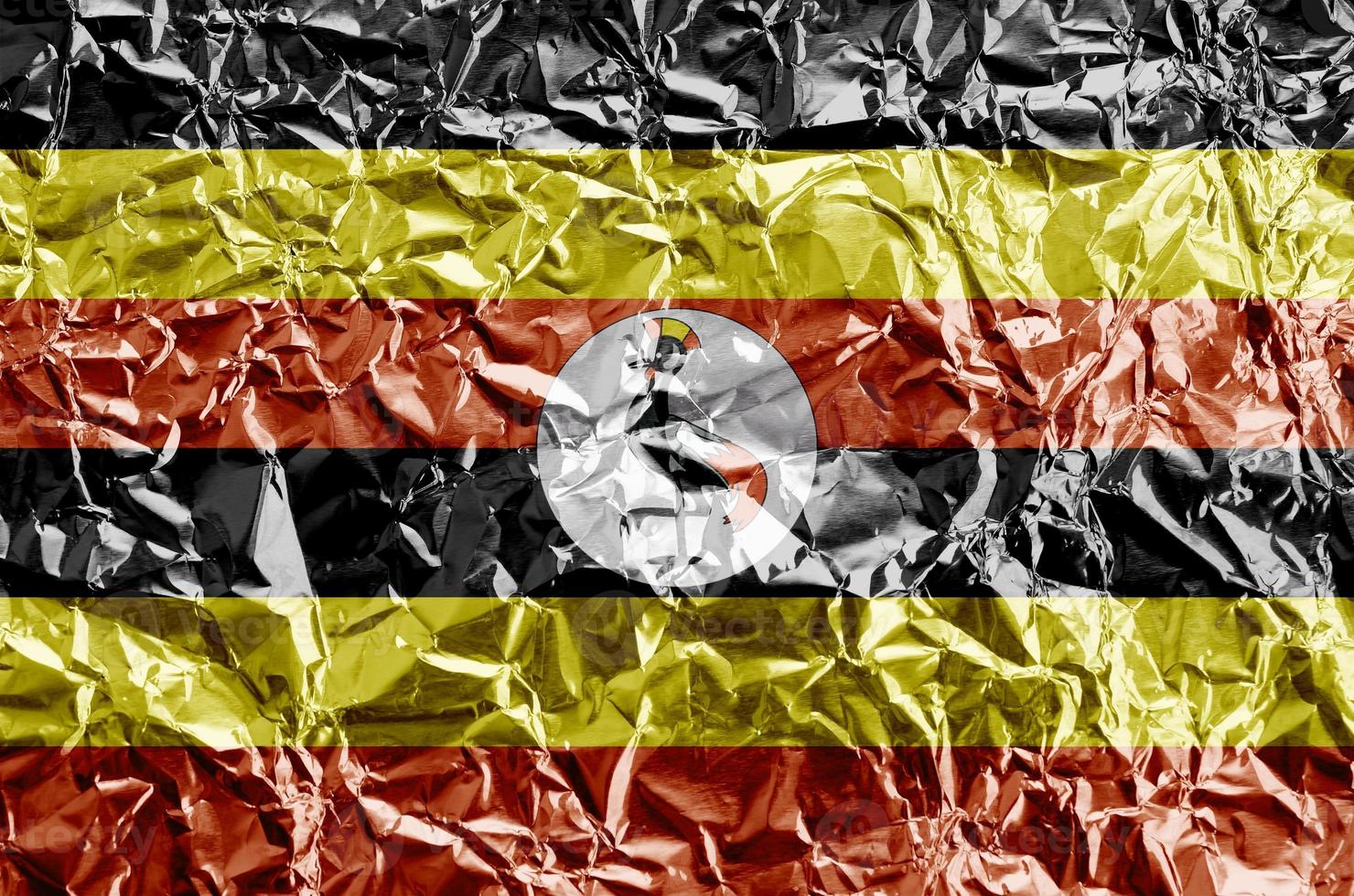 Uganda flag depicted in paint colors on shiny crumpled aluminium foil closeup. Textured banner on rough background photo