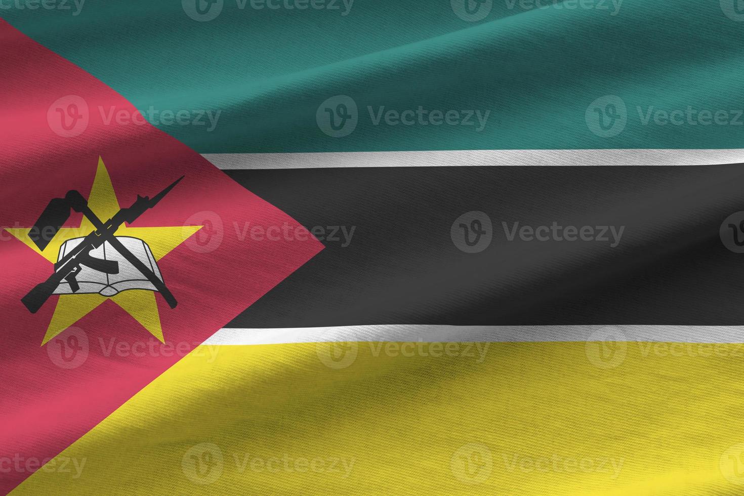 Mozambique flag with big folds waving close up under the studio light indoors. The official symbols and colors in banner photo