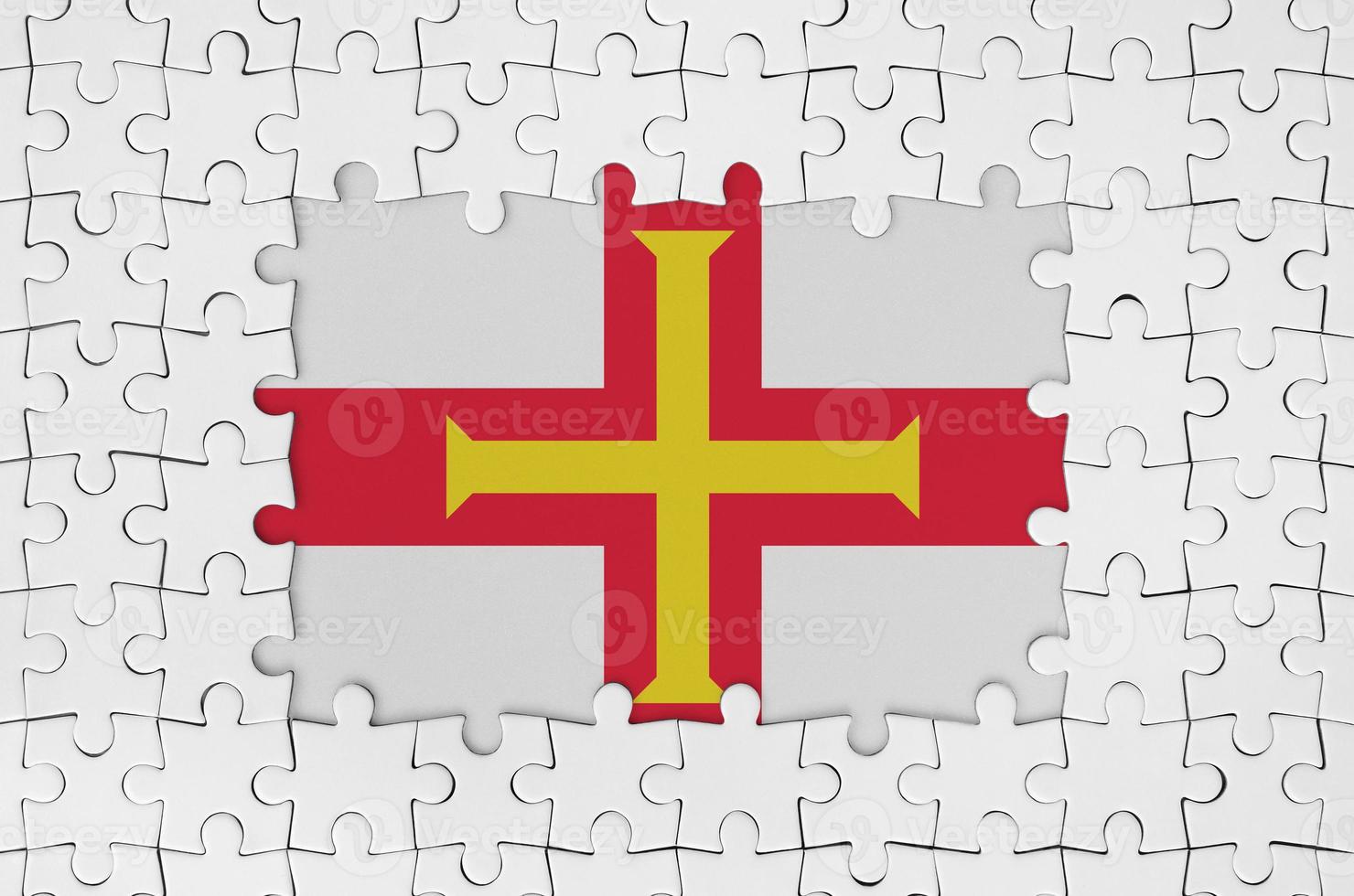 Guernsey flag in frame of white puzzle pieces with missing central part photo