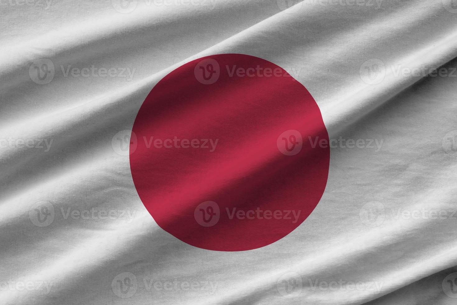 Japan flag with big folds waving close up under the studio light indoors. The official symbols and colors in banner photo