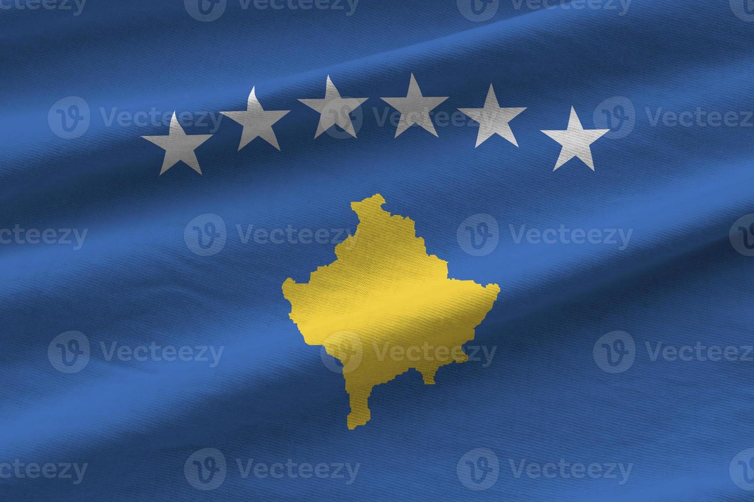 Kosovo flag with big folds waving close up under the studio light indoors. The official symbols and colors in banner photo