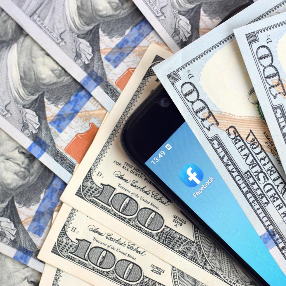 Smartphone screen with Facebook app and lot of hundred dollar bills. Business and social networking concept photo
