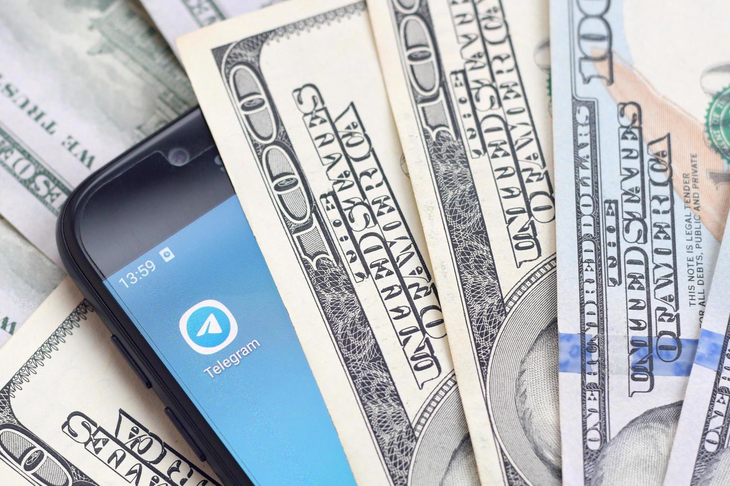 Smartphone screen with Telegram app and lot of hundred dollar bills. Business and social networking concept photo