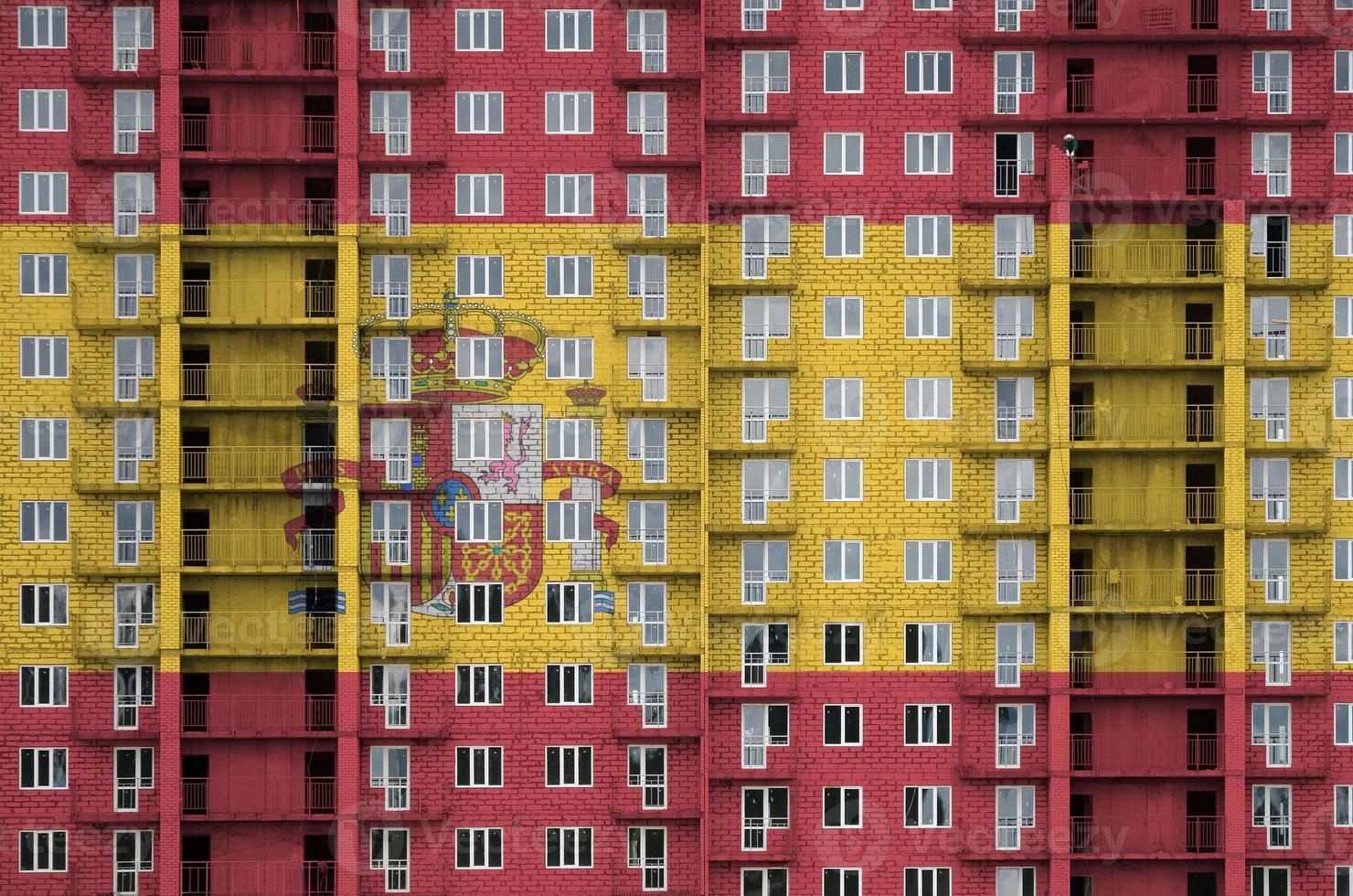 Spain flag depicted in paint colors on multi-storey residental building under construction. Textured banner on brick wall background photo