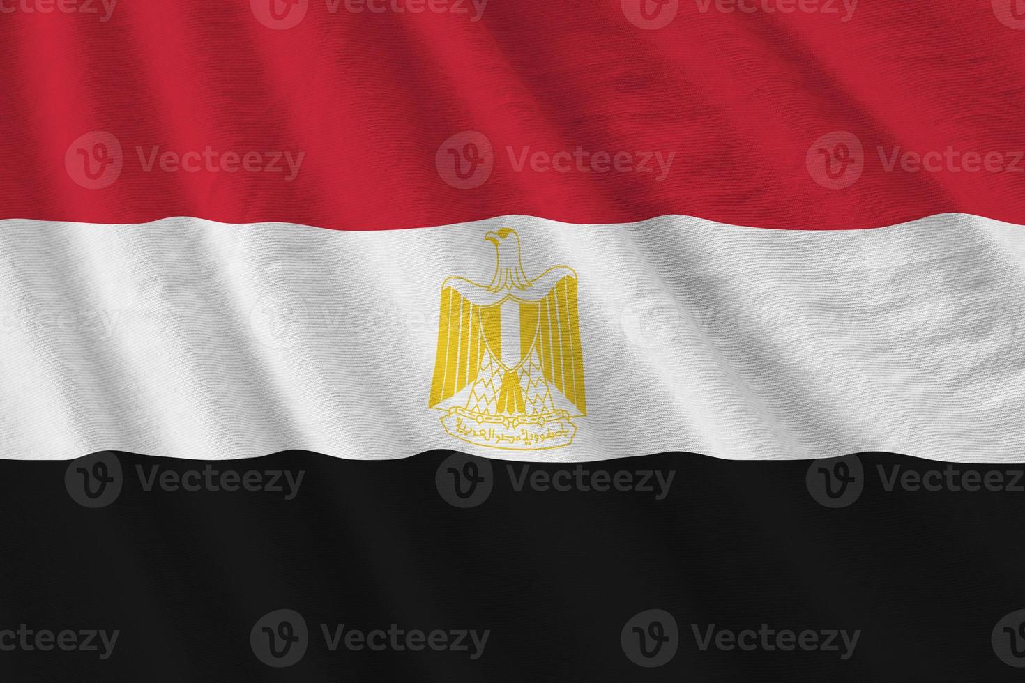 Egypt flag with big folds waving close up under the studio light indoors. The official symbols and colors in banner photo