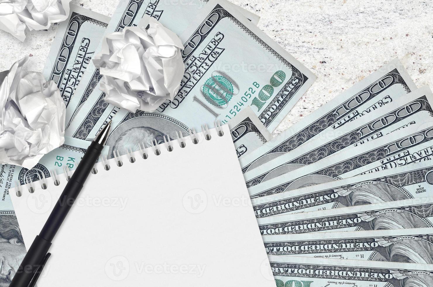 100 US dollars bills and balls of crumpled paper with blank notepad. Bad ideas or less of inspiration concept. Searching ideas for investment photo