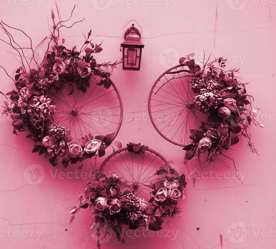 Decoration urban art object from bicycle wheels and flowers on wall Image toned in Viva Magenta, color of the 2023 year photo