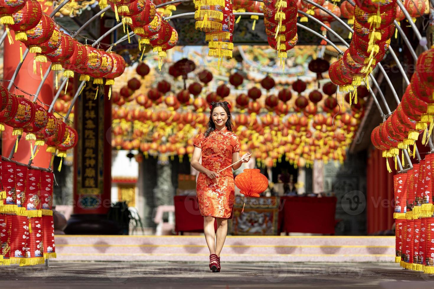 mujer asiática con vestido rojo cheongsam qipao sosteniendo una linterna mientras visita el templo budista chino durante el año nuevo lunar por el concepto de cultura tradicional foto