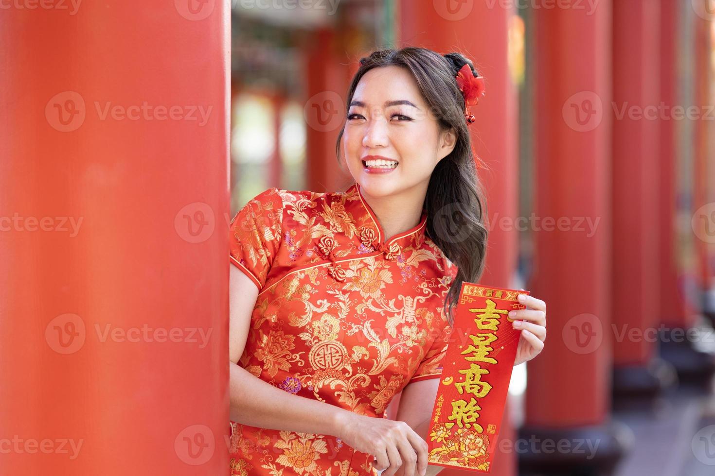 Asian woman in red cheongsam qipao dress is holding blessing fortune card saying 'to be blessed by a lucky star' inside Chinese Buddhist temple during lunar new year for best wish and good luck photo