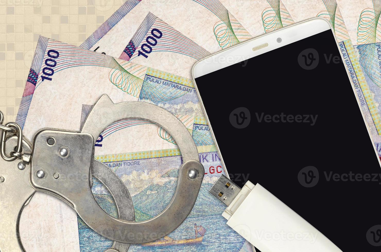 Billetes de 1000 rupias indonesias y teléfono inteligente con esposas policiales. concepto de ataques de phishing de piratas informáticos, estafa ilegal o distribución blanda de malware foto