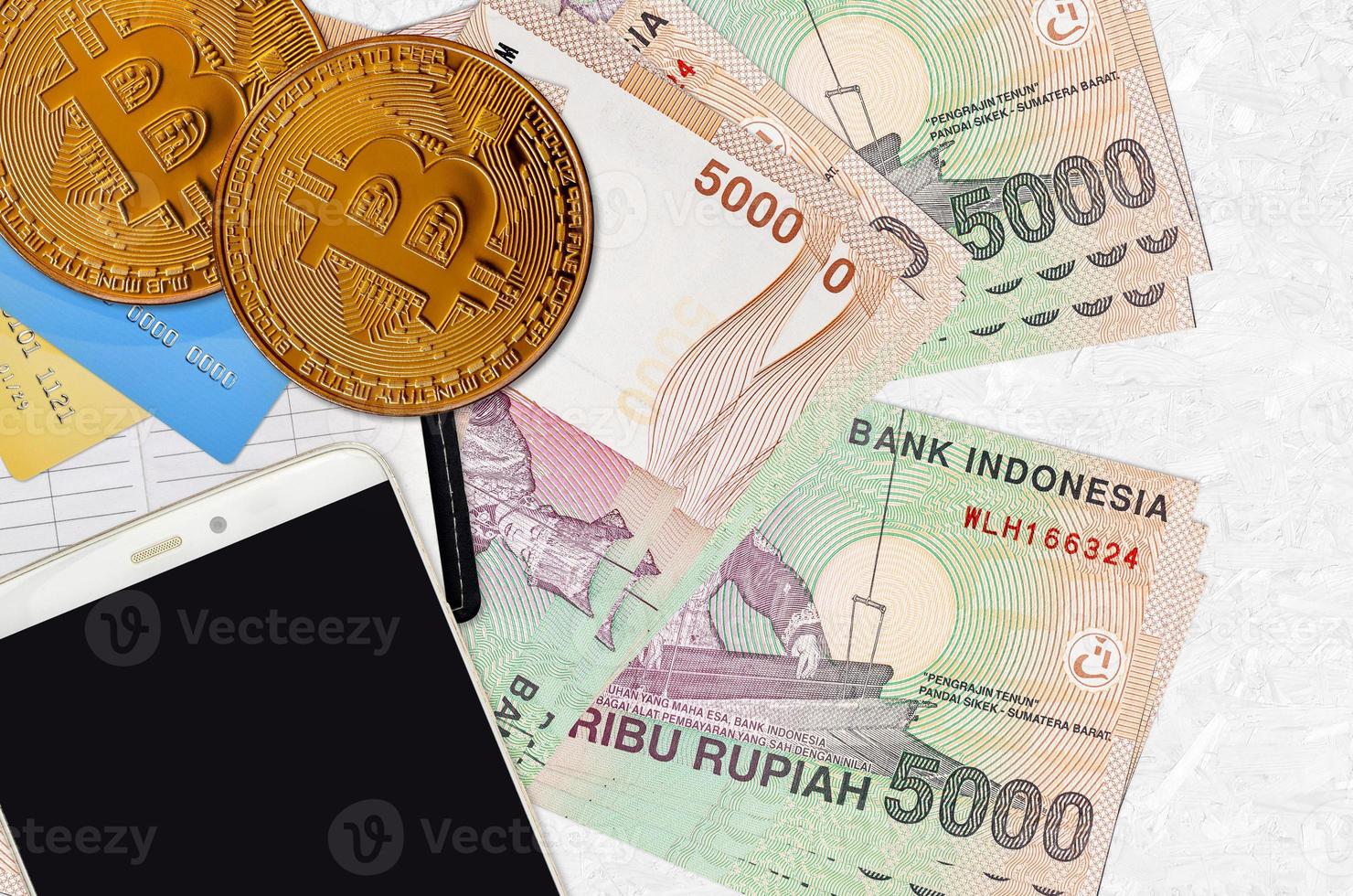 5000 Indonesian rupiah bills and golden bitcoins with smartphone and credit cards. Cryptocurrency investment concept. Crypto mining or trading photo