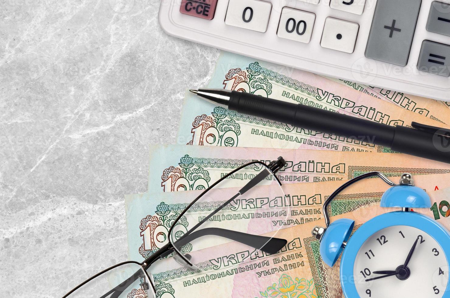 100 Ukrainian hryvnias bills and calculator with glasses and pen. Business loan or tax payment season concept. Time to pay taxes photo