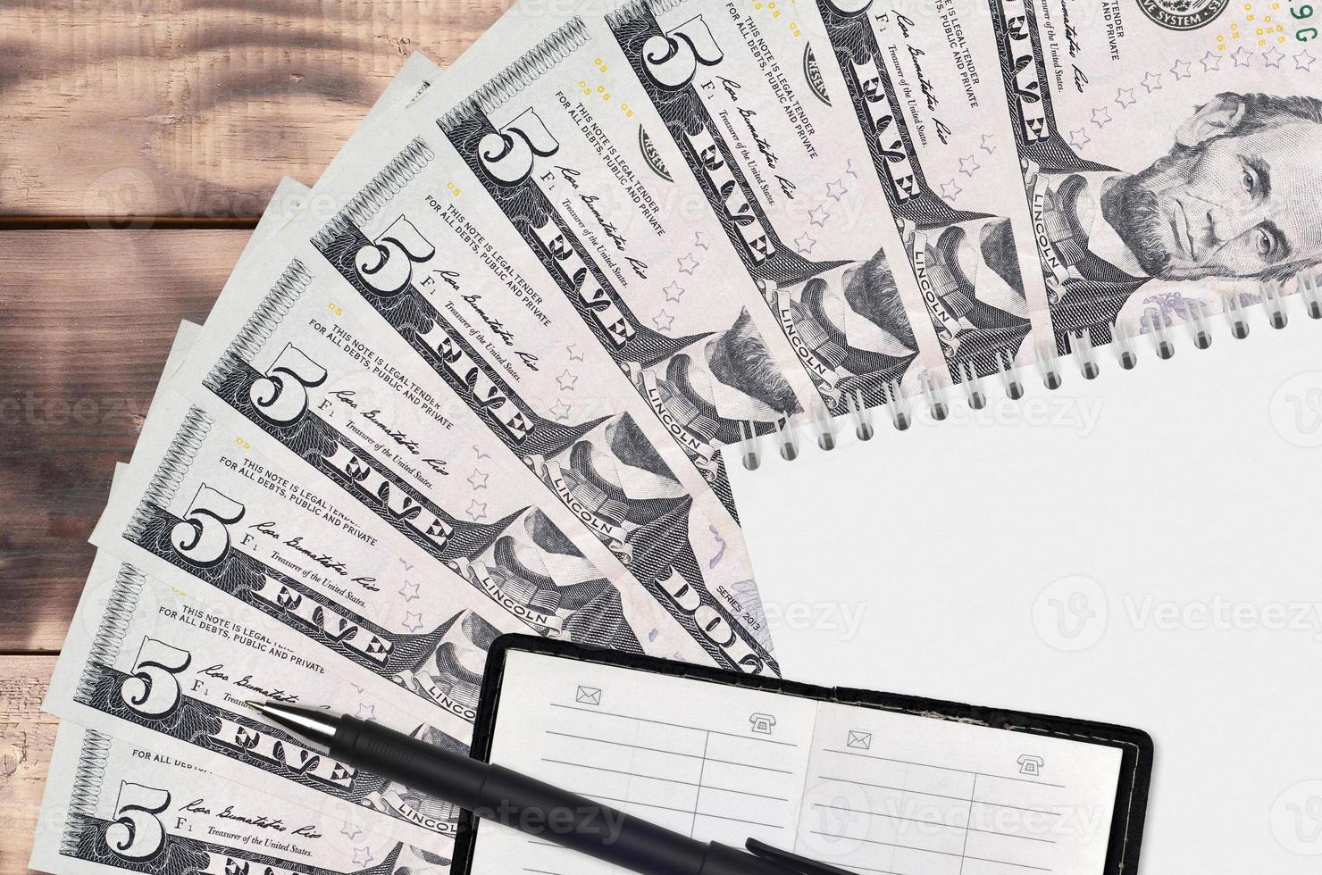 5 US dollars bills fan and notepad with contact book and black pen. Concept of financial planning and business strategy photo