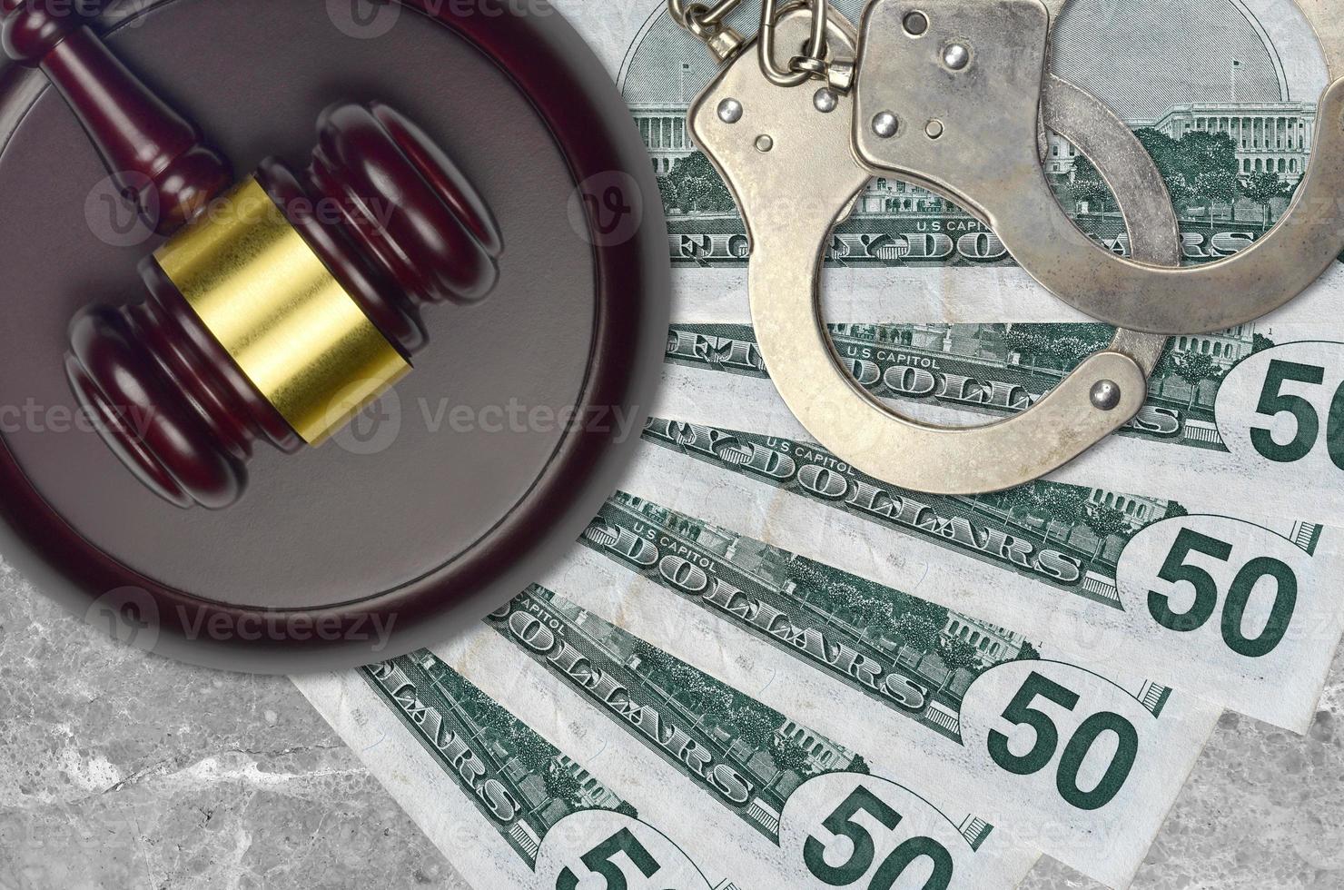 50 US dollars bills and judge hammer with police handcuffs on court desk. Concept of judicial trial or bribery. Tax avoidance photo