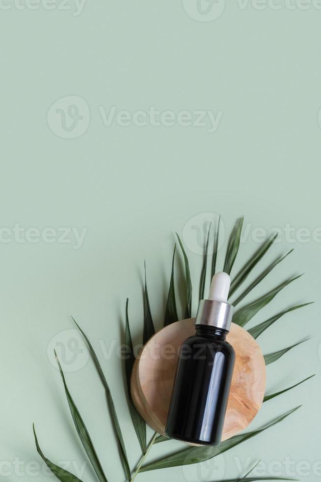 Cosmetic bottle with pipette on wooden slice  top view, flat lay on colored background with nature decoration. Natural cosmetic concept photo